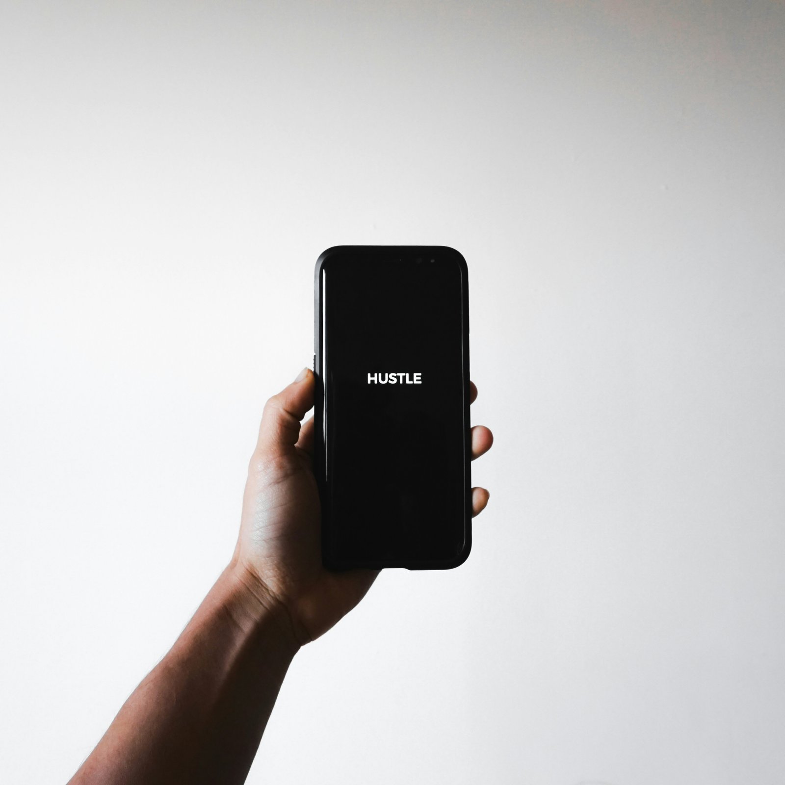 Man holding a phone with 'Hustle' displayed on the screen, symbolizing online side hustles